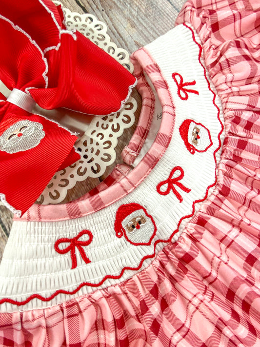 Close-up of a white smocked collar on a red and pink plaid Christmas dress, embroidered with two Santa Claus faces and 3 red bows. The detailed stitching are clearly visible, emphasizing the festive and delicate craftsmanship. - Alternative view
