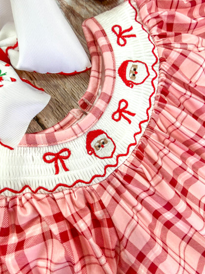 Close-up of a white smocked collar on an infant romper, embroidered with 2 Santa Claus faces and 3 red bows. The detailed stitching emphasizing the festive and delicate craftsmanship.
