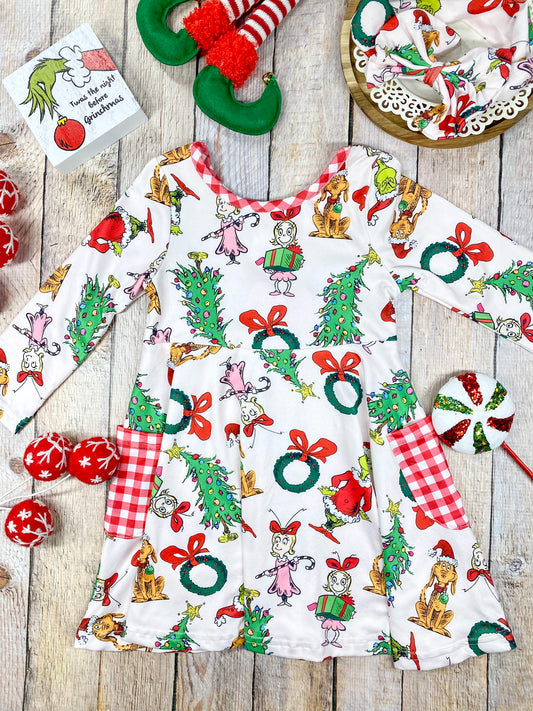 Girls’ long sleeve Christmas twirl dress featuring an all-over Grinch character print on white, with red and white gingham-trimmed pockets and matching neckline. Made from soft, stretchy knit fabric and cut for a twirl-friendly silhouette—perfect for holiday parties and photos.