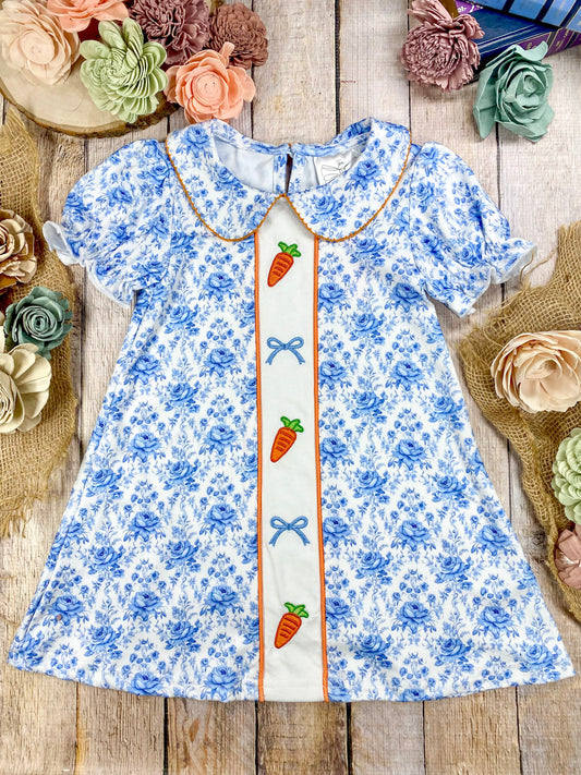 Blue floral dress with carrot and bow design on a wooden surface with flowers around