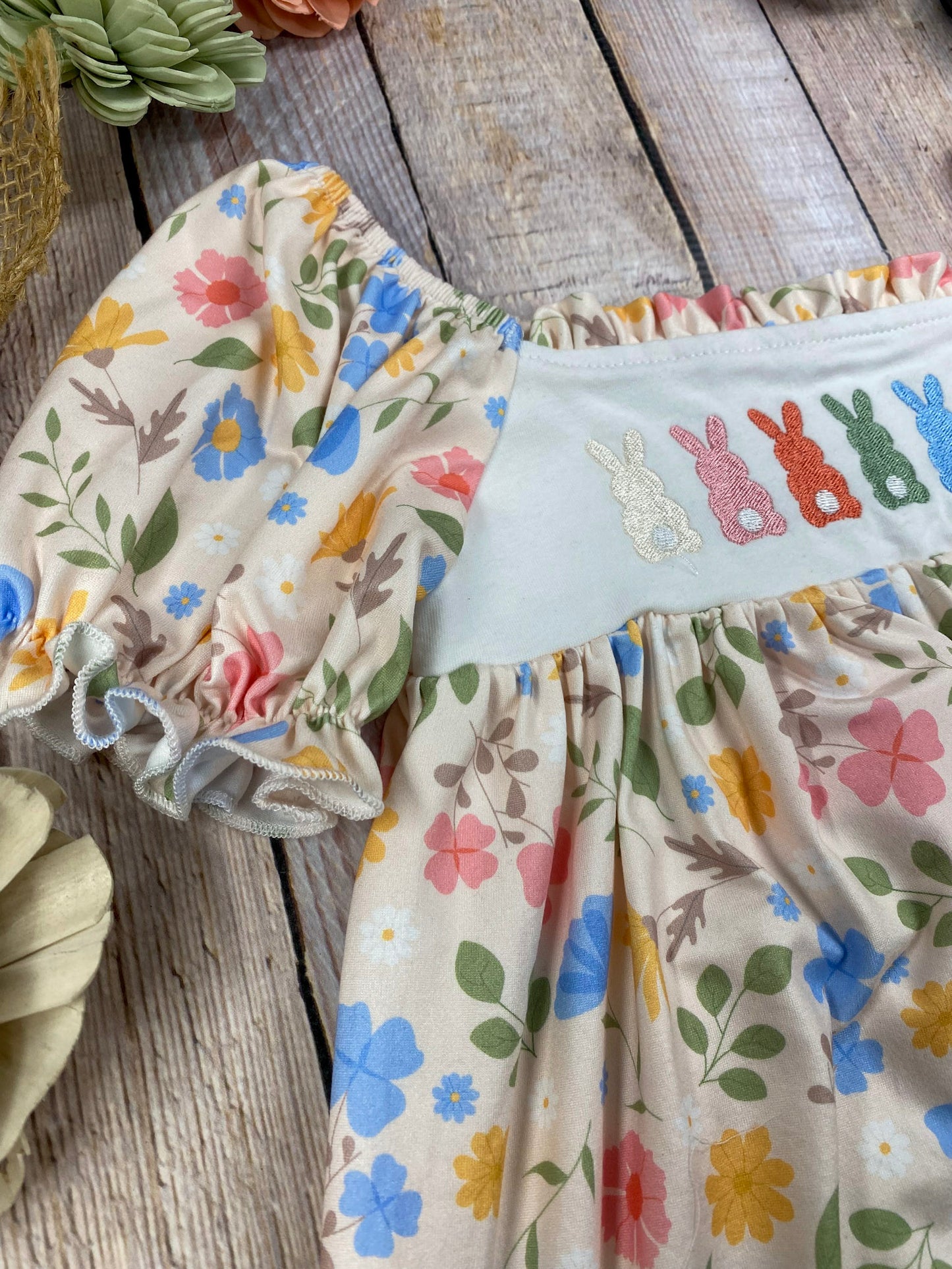 zoom in on Children's outfit with floral top and bunny print pants on a wooden surface