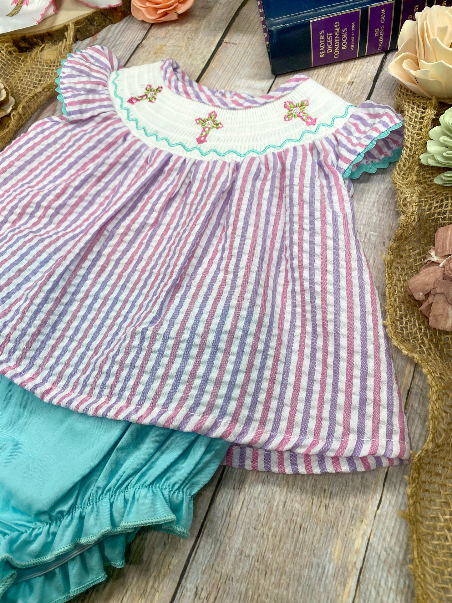 Striped top with cross embroidery and turquoise ruffled bottom on a wooden surface.