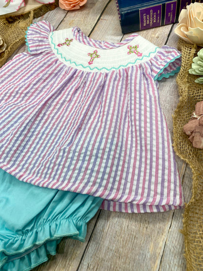 Striped top with cross embroidery and turquoise ruffled bottom on a wooden surface.