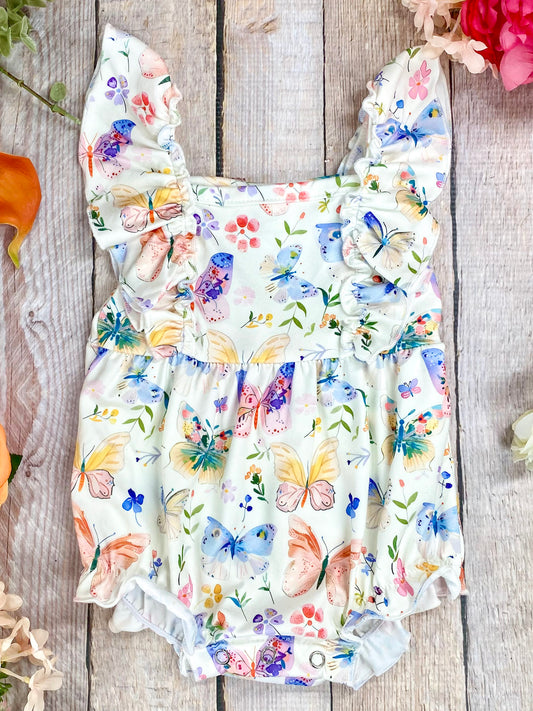 butterfly baby romper on a wooden surface with flowers around