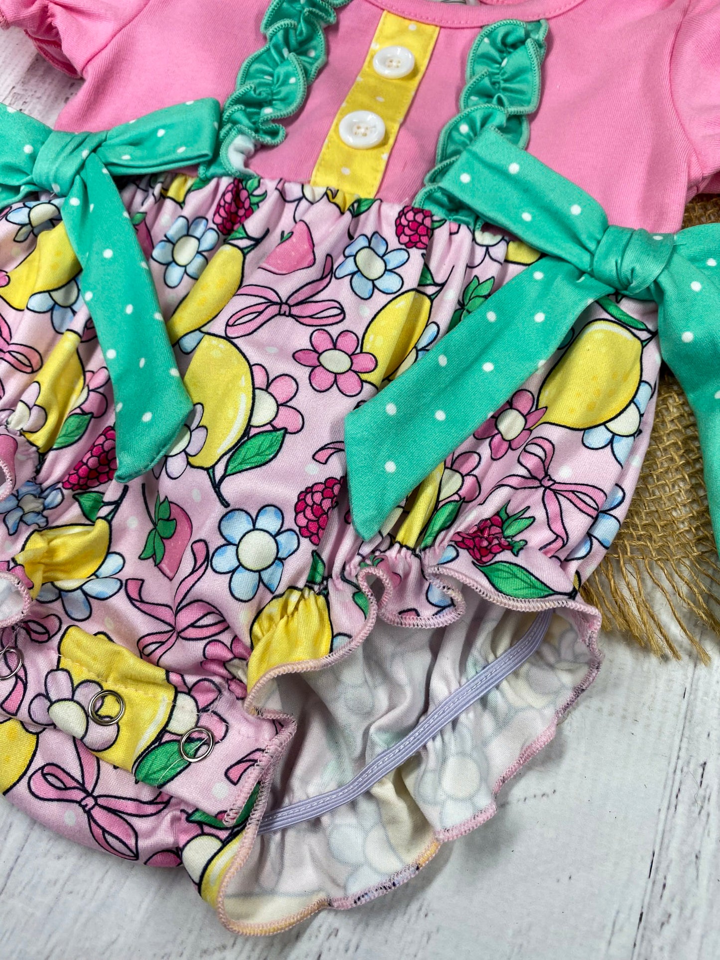 lemon and bows baby romper on a white marble background