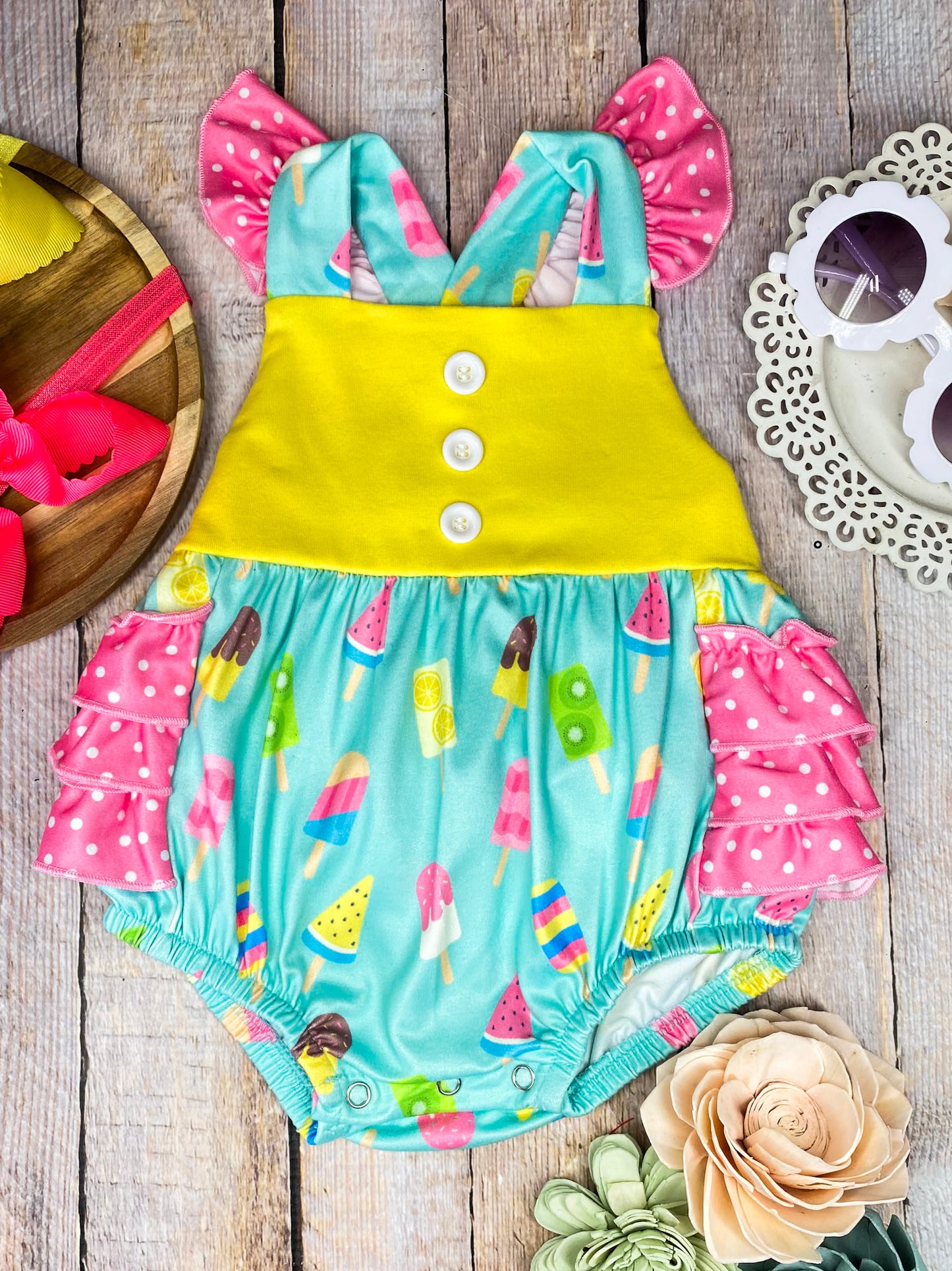 Colorful baby romper with ice cream pattern on a wooden background