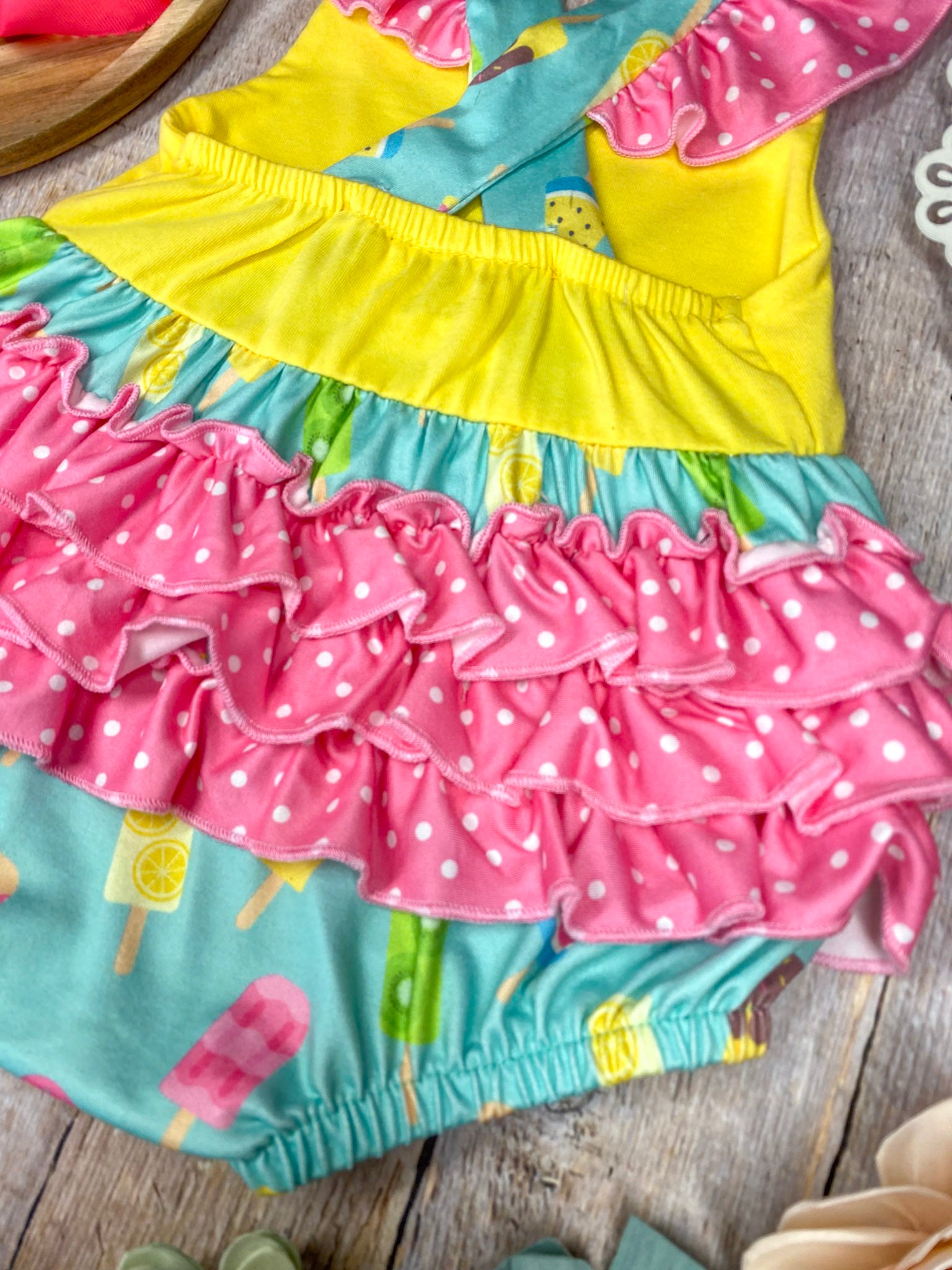 Colorful baby romper with ice cream pattern on a wooden background