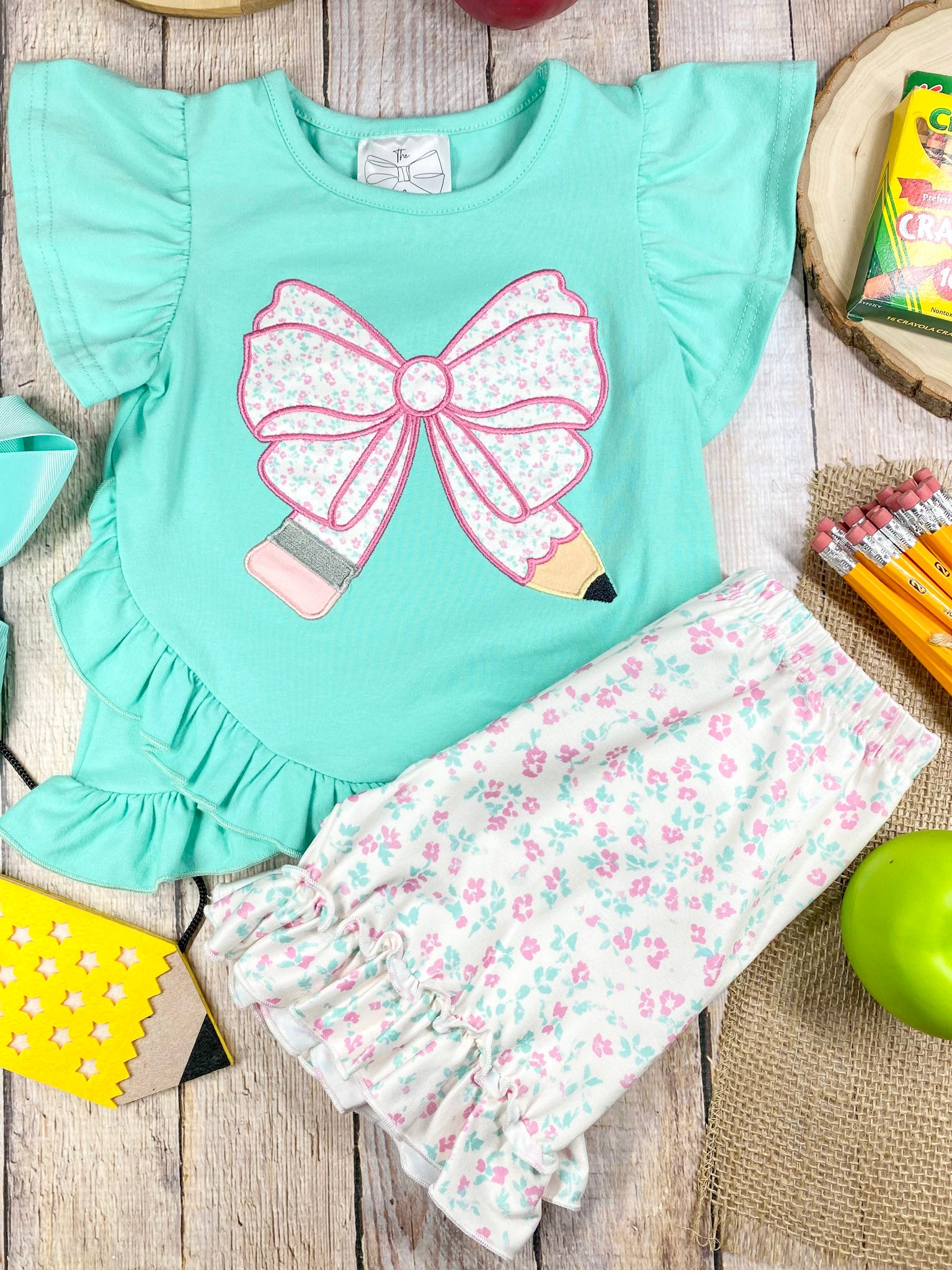 Children's outfit with green pencil top and floral shorts on a wooden background