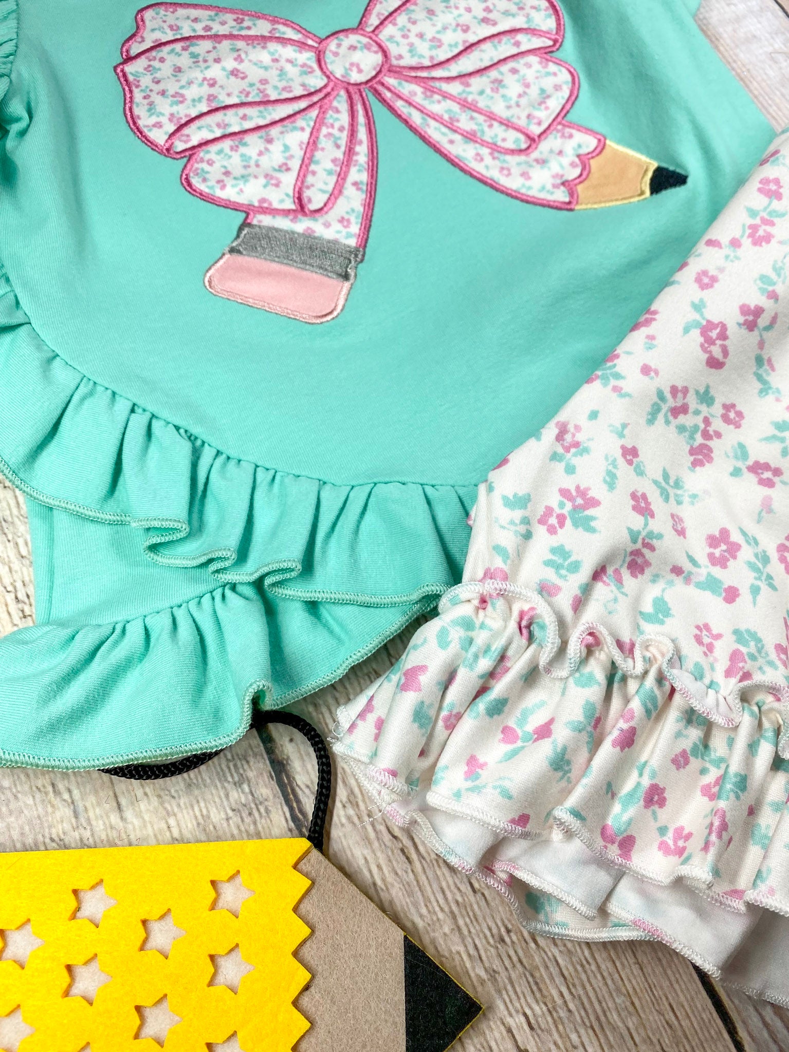 Children's outfit with green pencil top and floral shorts on a wooden background