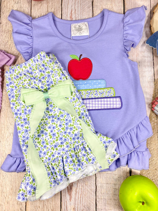 Children's outfit with purple top and floral shorts on a wooden background