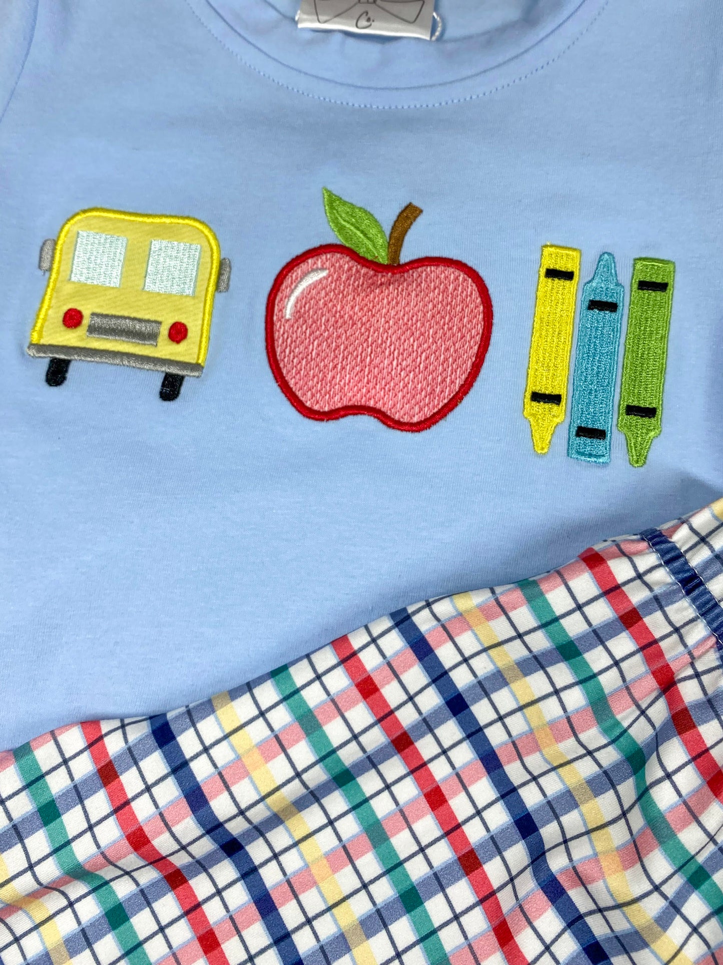 Children's outfit with light blue shirt and plaid shorts on a wooden background