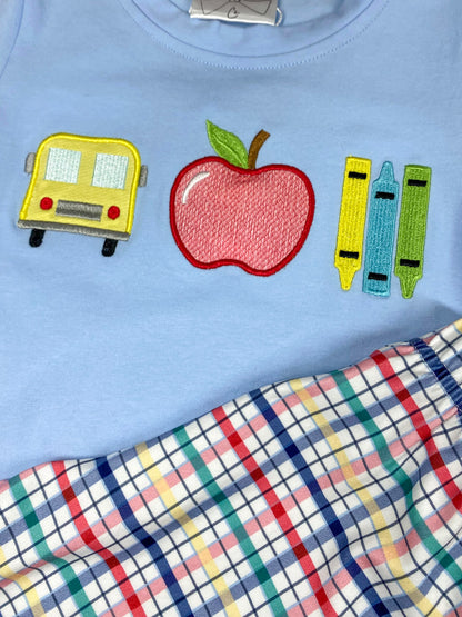 Children's outfit with light blue shirt and plaid shorts on a wooden background