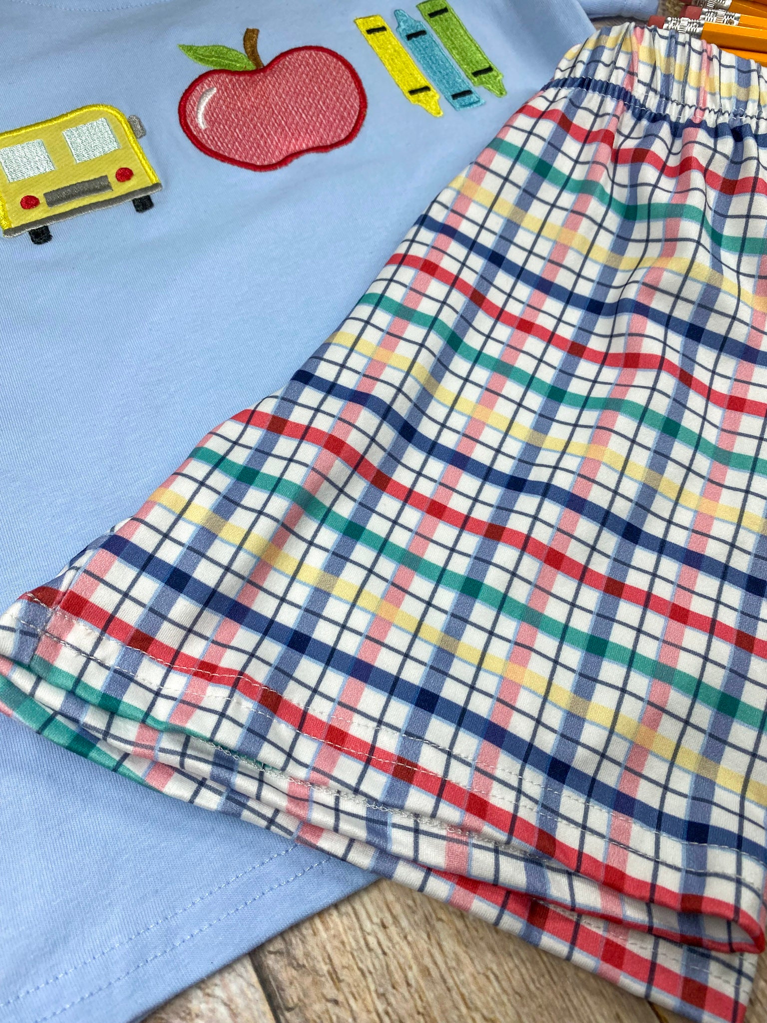 Children's outfit with light blue shirt and plaid shorts on a wooden background