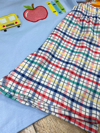 Children's outfit with light blue shirt and plaid shorts on a wooden background