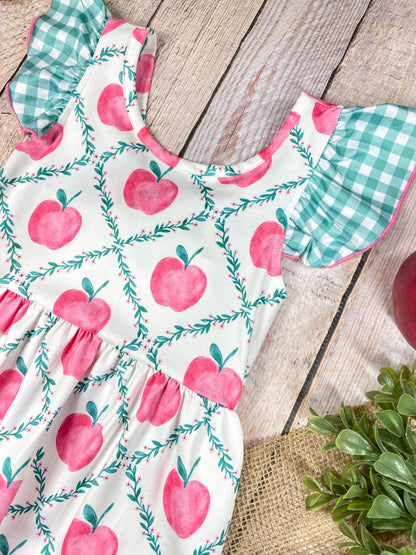 Children's dress with pink apple pattern on a wooden background