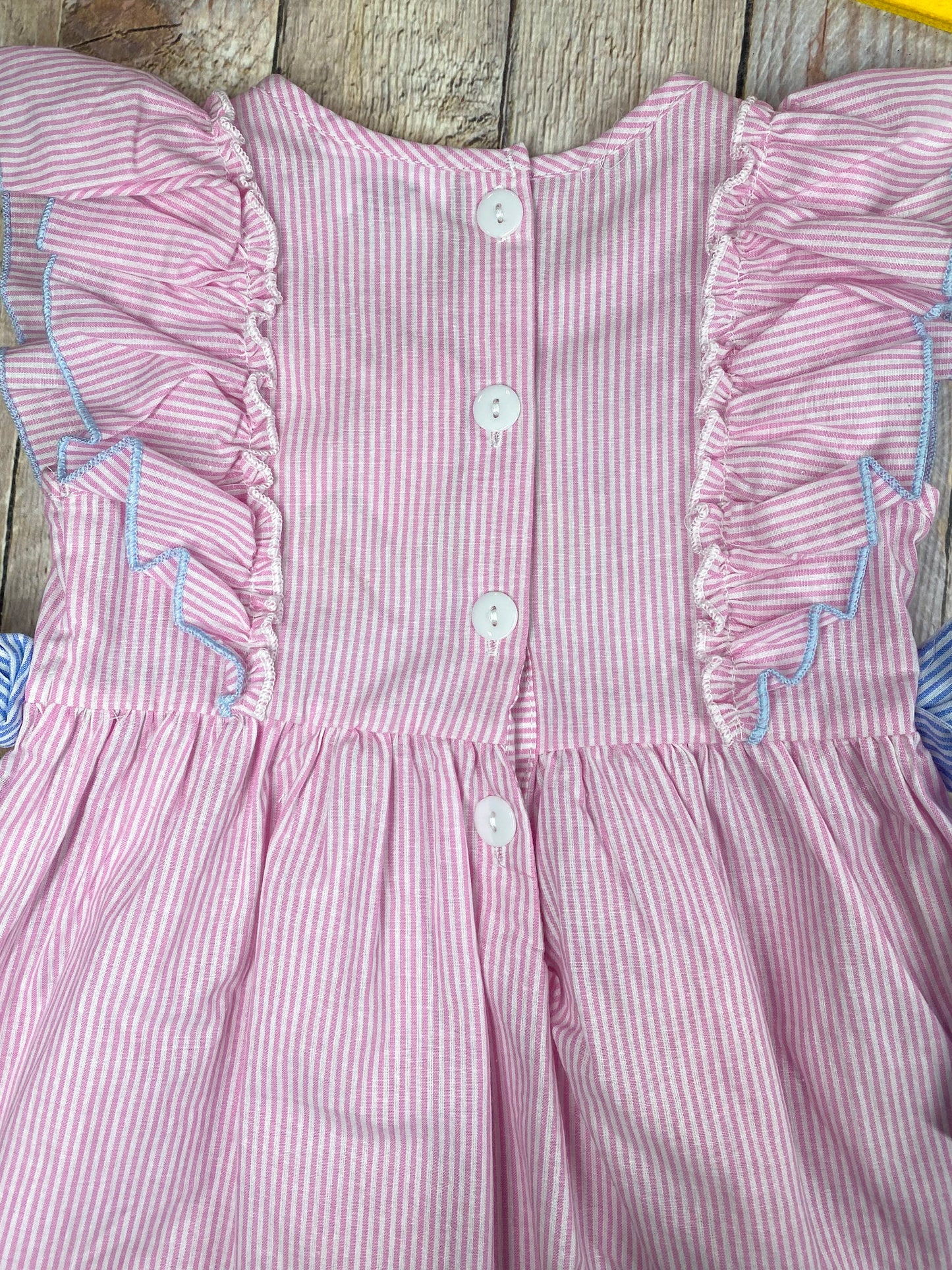 Pink striped dress with a bow on a wooden background