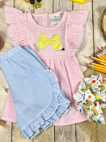 Pink dress with ruffled sleeves and blue shorts on a wooden background