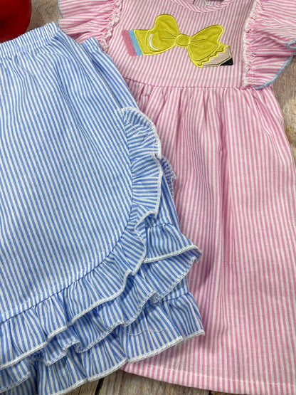 Pink dress with ruffled sleeves and blue shorts on a wooden background