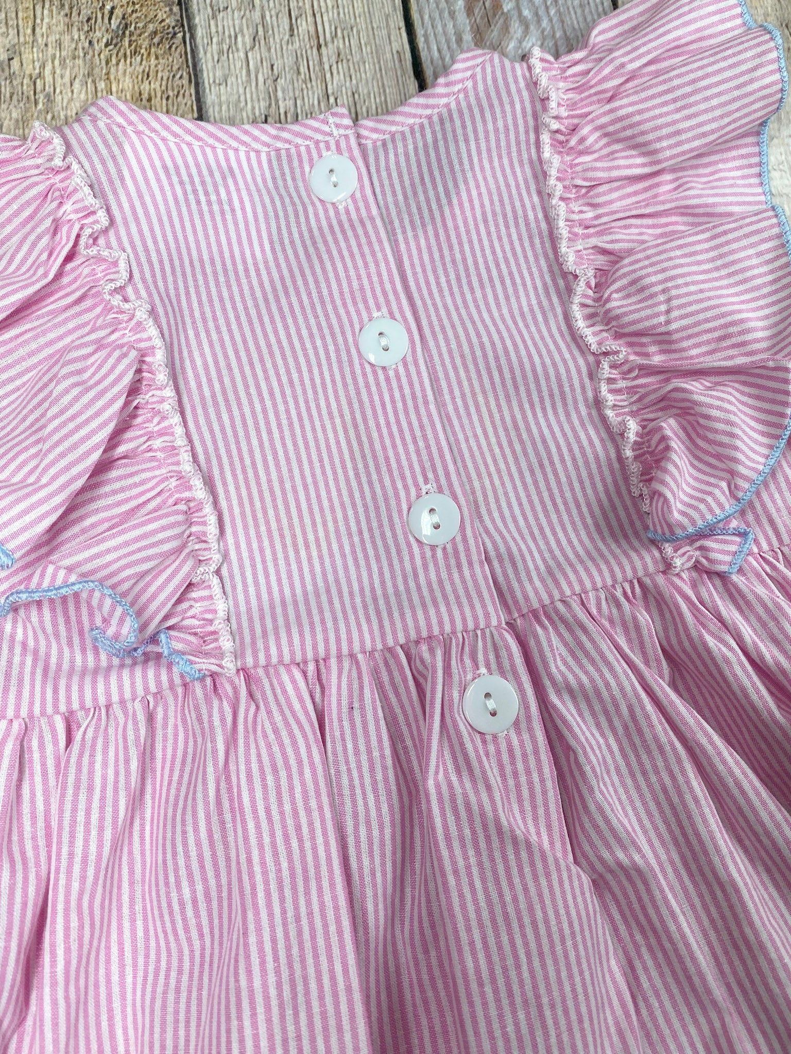 Pink dress with ruffled sleeves and blue shorts on a wooden background