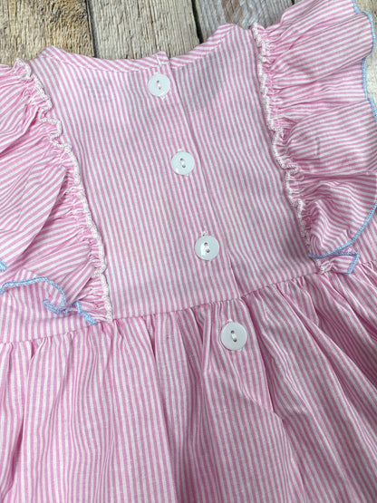 Pink dress with ruffled sleeves and blue shorts on a wooden background