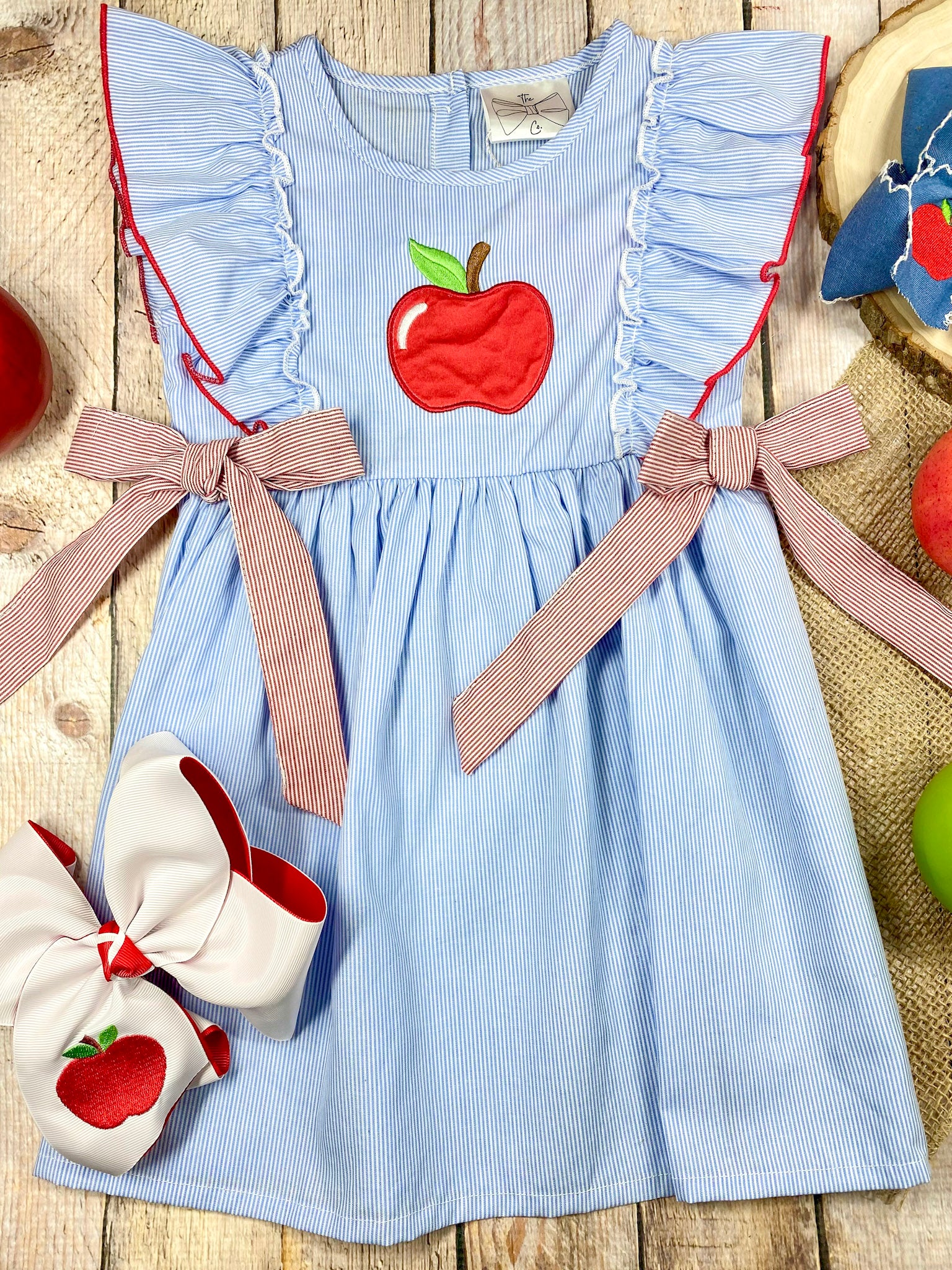 Blue dress with red apple design and pink accents on a wooden background
