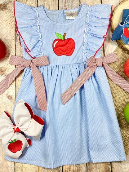Blue dress with red apple design and pink accents on a wooden background