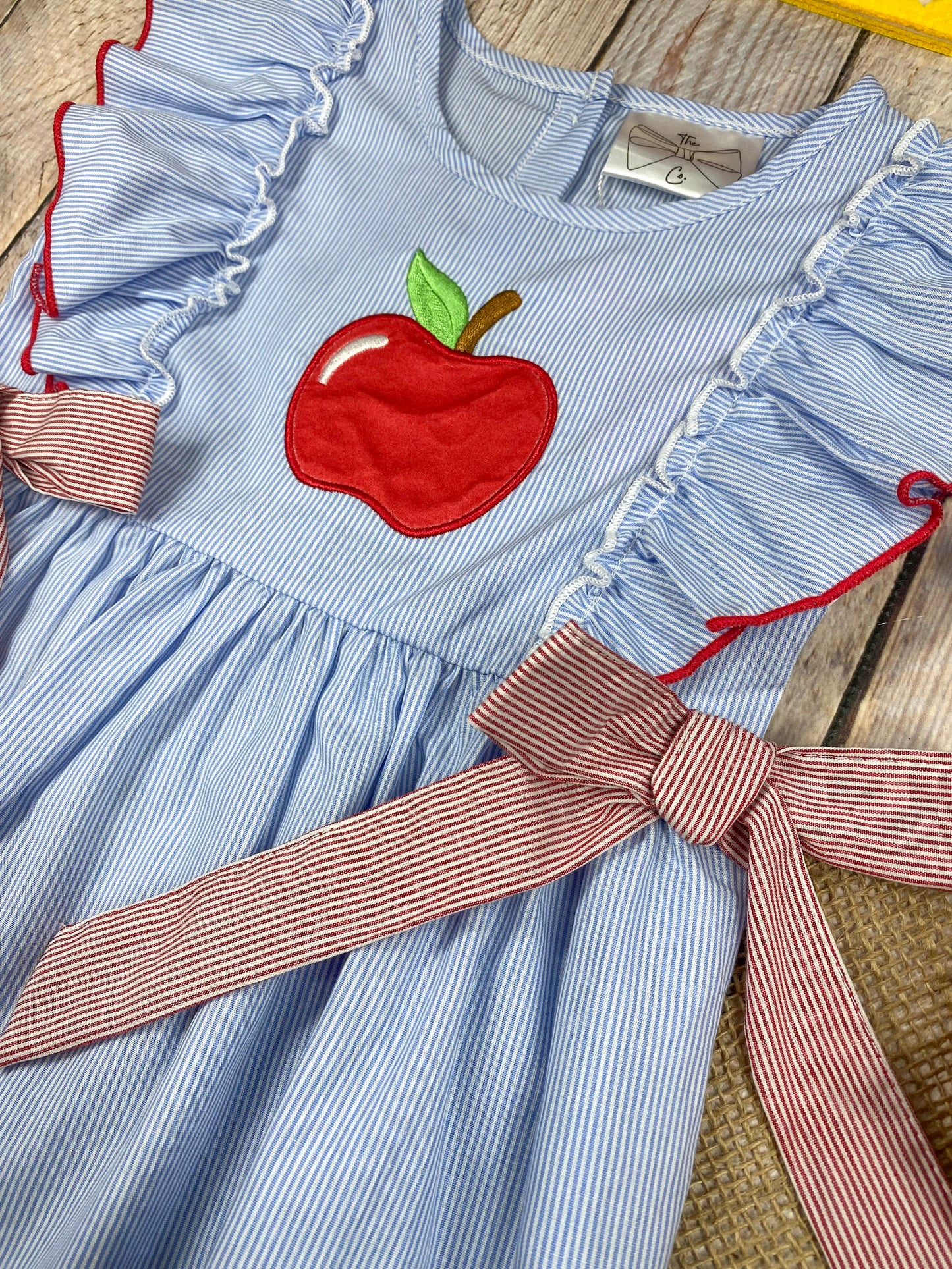 Blue dress with red apple design and pink accents on a wooden background