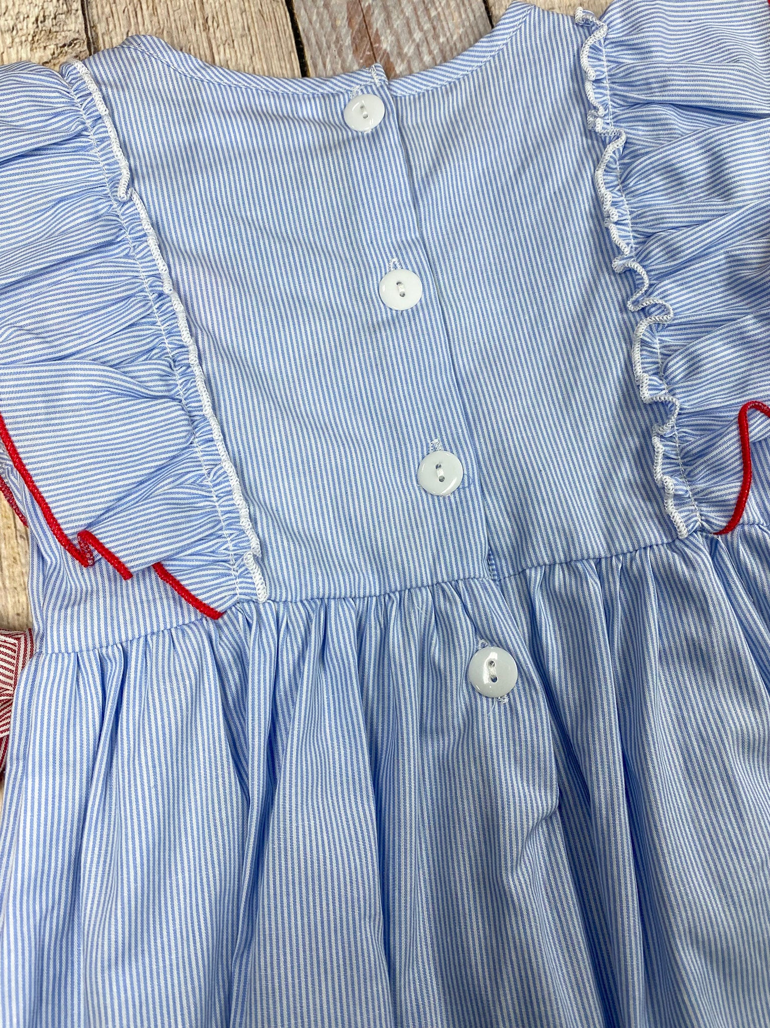 Blue dress with red apple design and pink accents on a wooden background