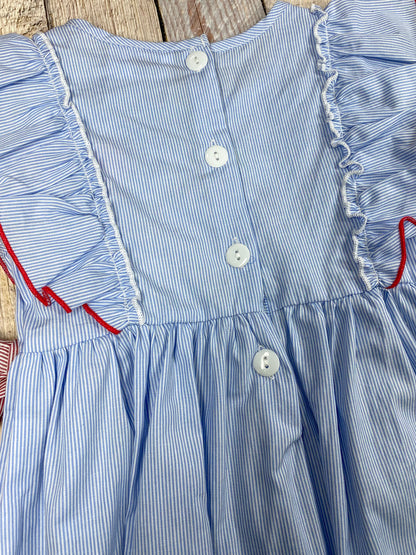 Blue dress with red apple design and pink accents on a wooden background