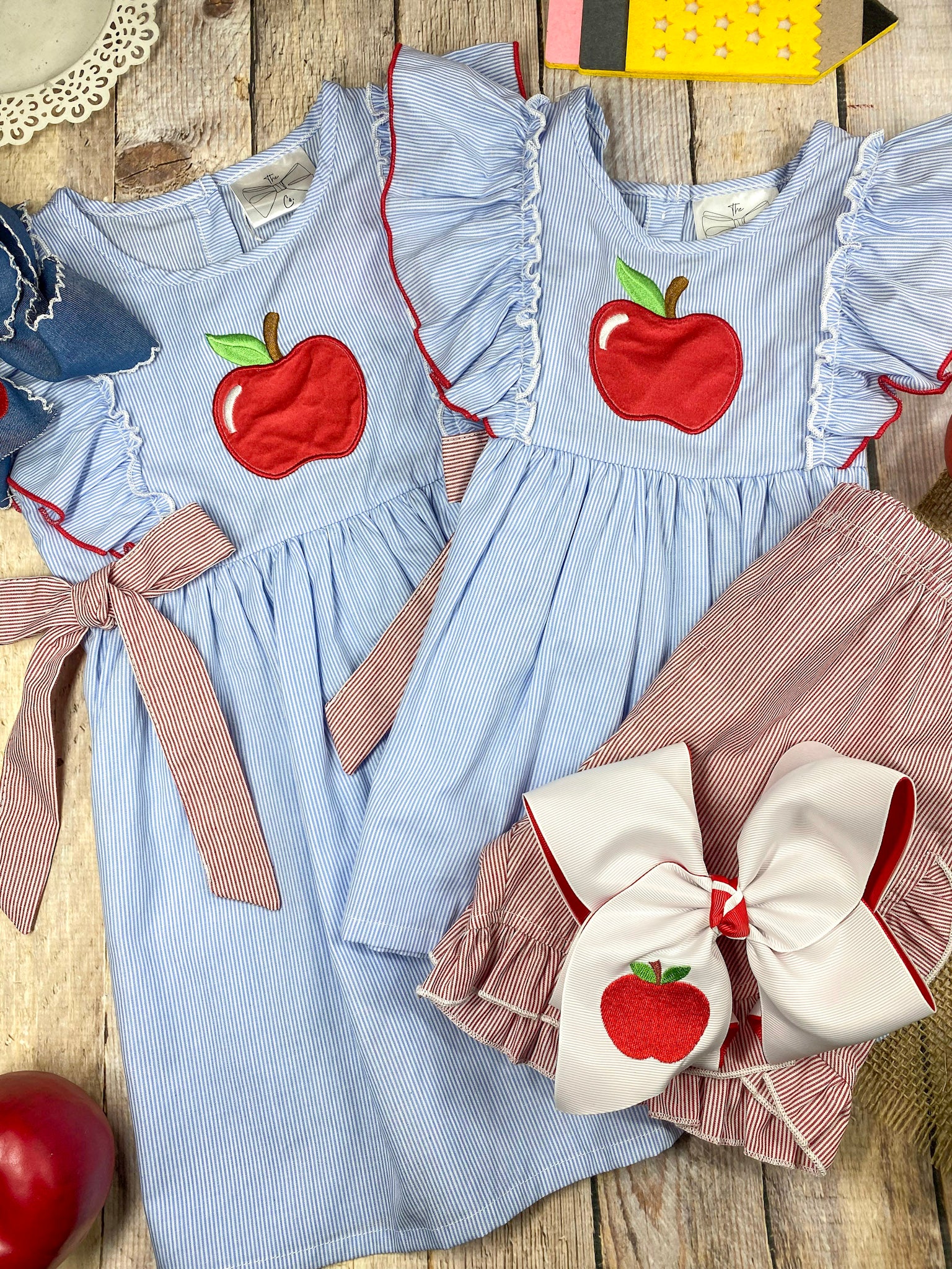 Blue dress with red apple design and pink accents on a wooden background