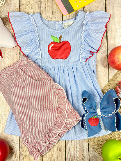 Children's outfit with blue top and pink shorts featuring an apple design on a wooden background