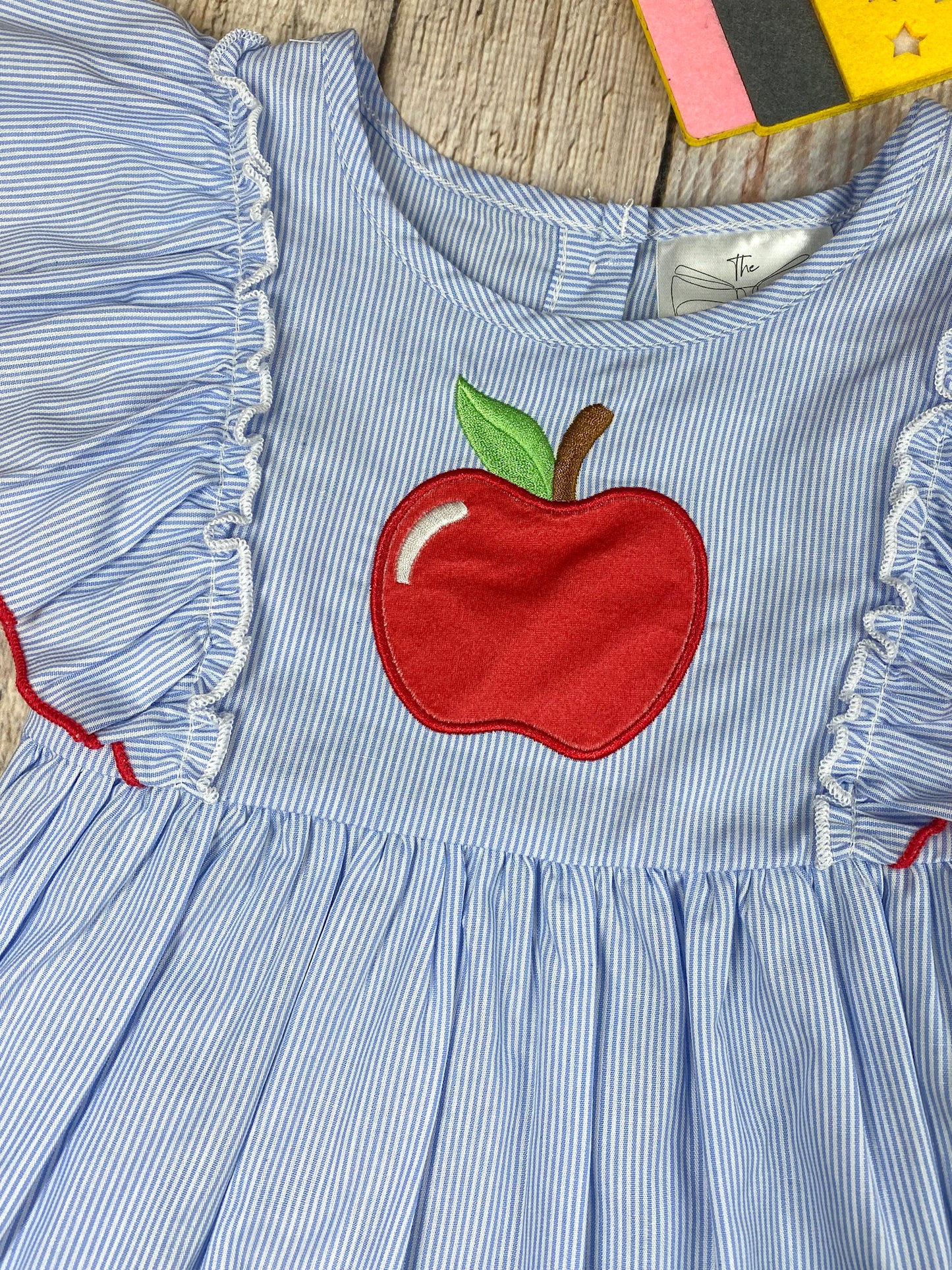 Children's outfit with blue top and pink shorts featuring an apple design on a wooden background