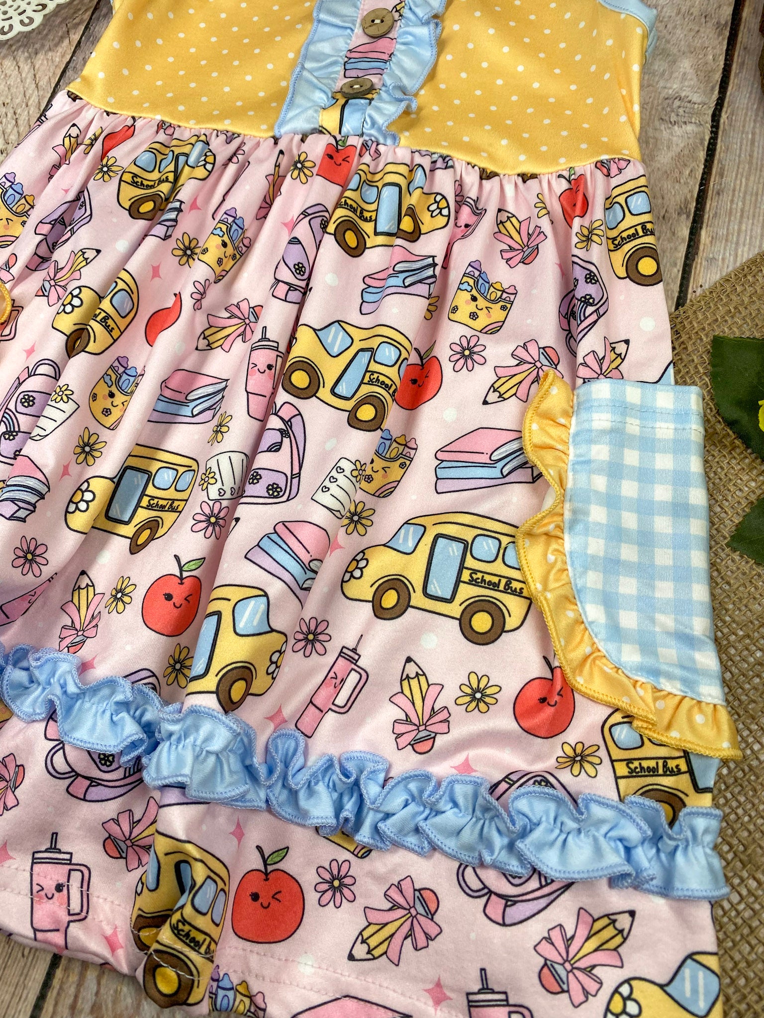 Colorful children's dress with cartoon bus and apple pattern on a wooden background