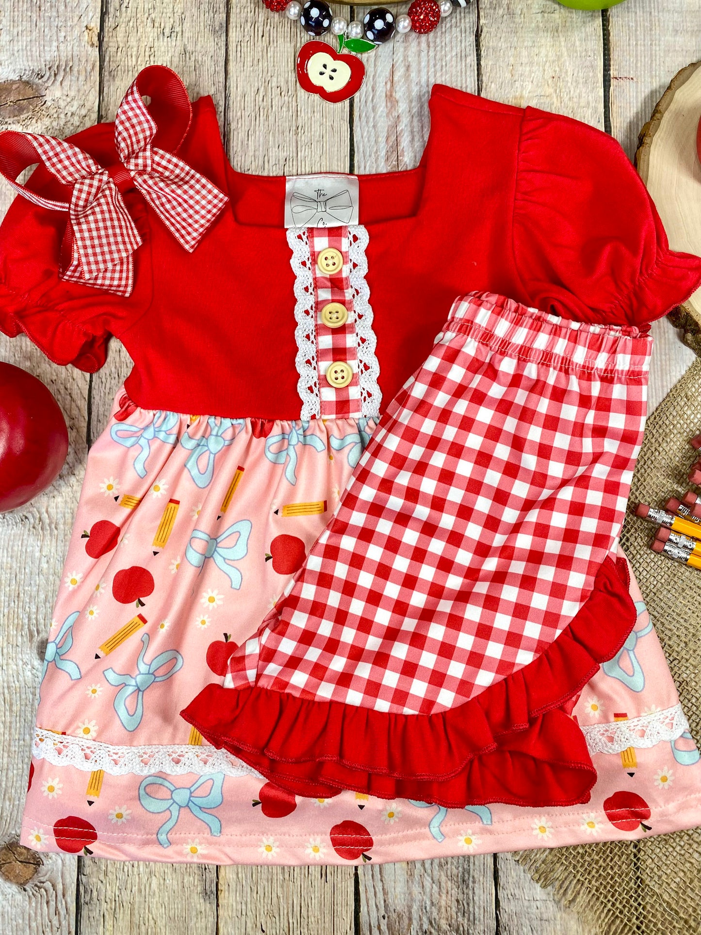 Red and pink children's outfit with checkered shorts on a wooden background