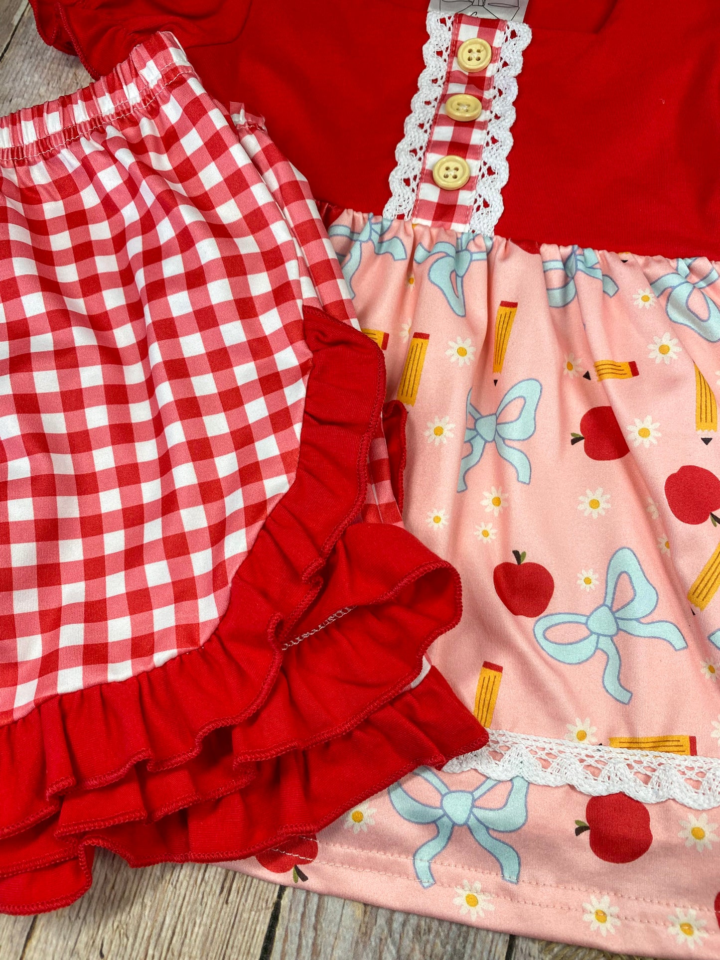 Red and pink children's outfit with checkered shorts on a wooden background