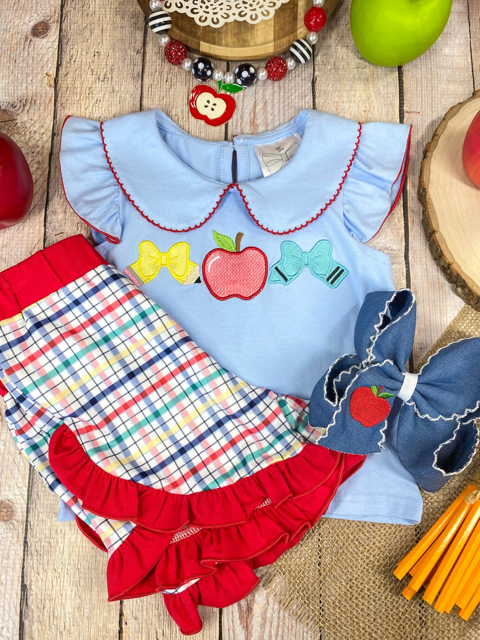 Children's outfit with light blue top and plaid shorts on a wooden background