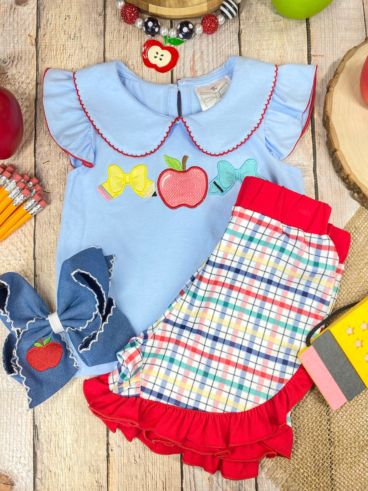 Children's outfit with light blue top and plaid shorts on a wooden background