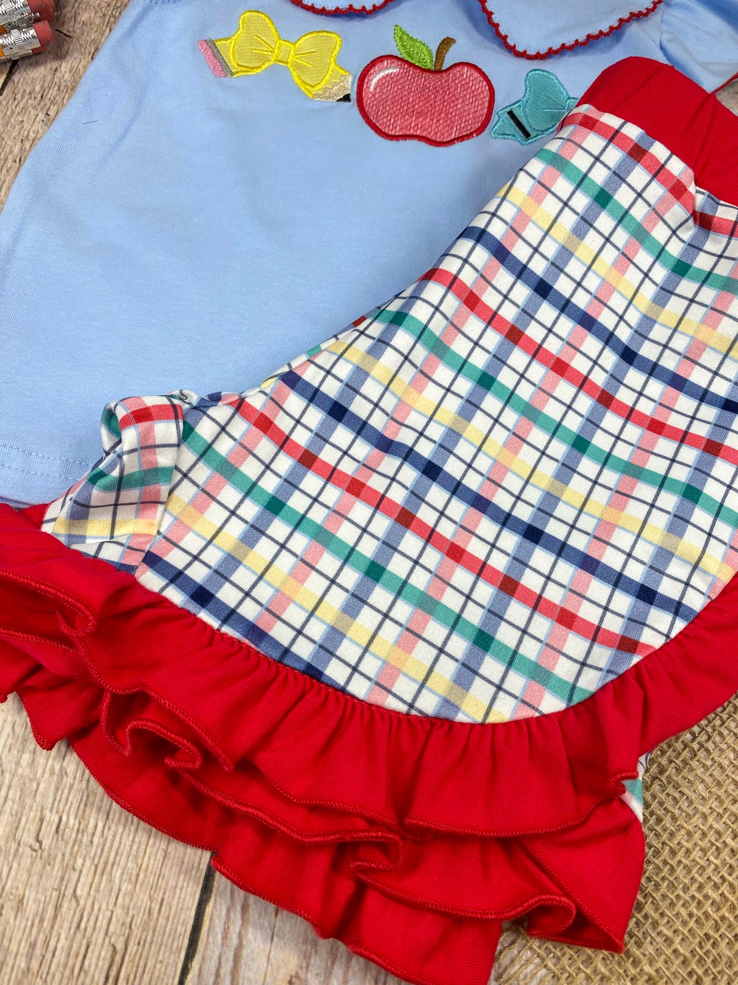 Children's outfit with light blue top and plaid shorts on a wooden background