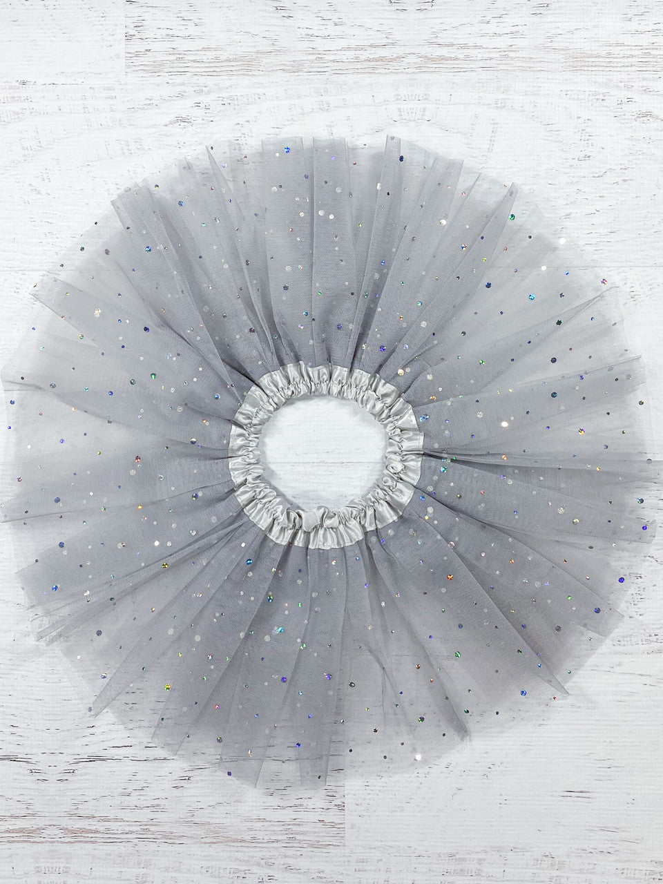 This soft grey tutu is made from polyester tulle, with a silver satin elastic waistband.  The top of three layers is covered with silver sparkle dots in varying sizes.  
