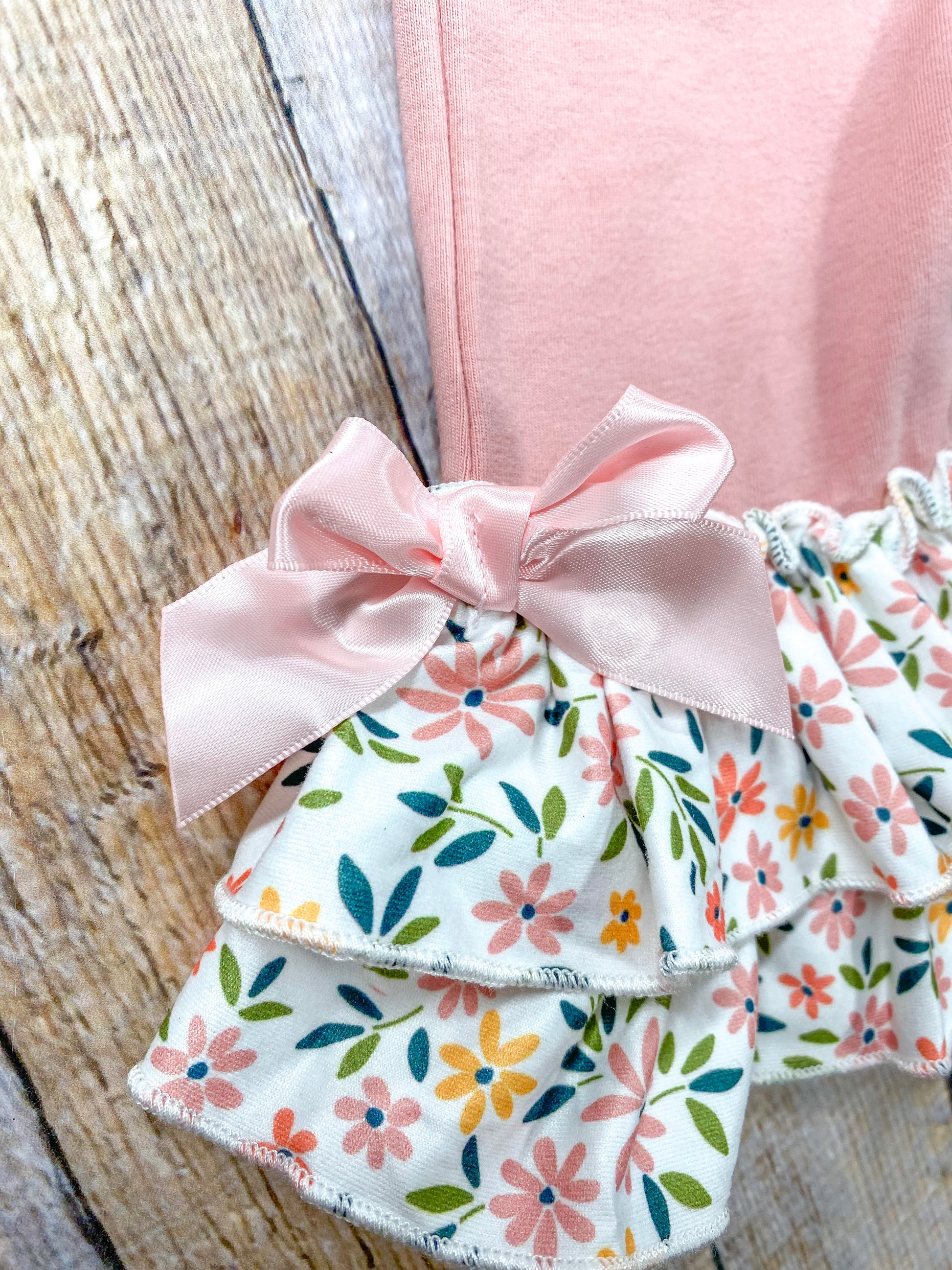 close up of end of pant leg showing double ruffles with floral pattern and a pink bow on side 
