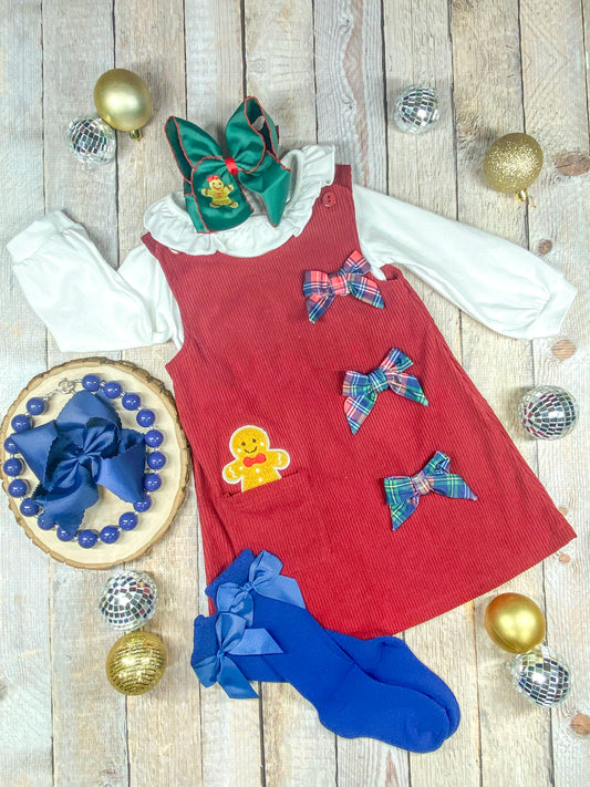 red corduroy dress with plaid bows and a gingerbread man applique coming out of the pocket and with a white long sleeve layered under the dress with ruffle collar