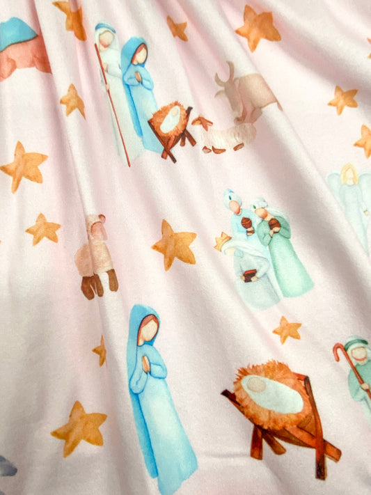 Detailed view of the pastel nativity scene print on a pink dress, featuring Mary, Joseph, baby Jesus in the manger, shepherds, animals, and gold stars. - Alternative view