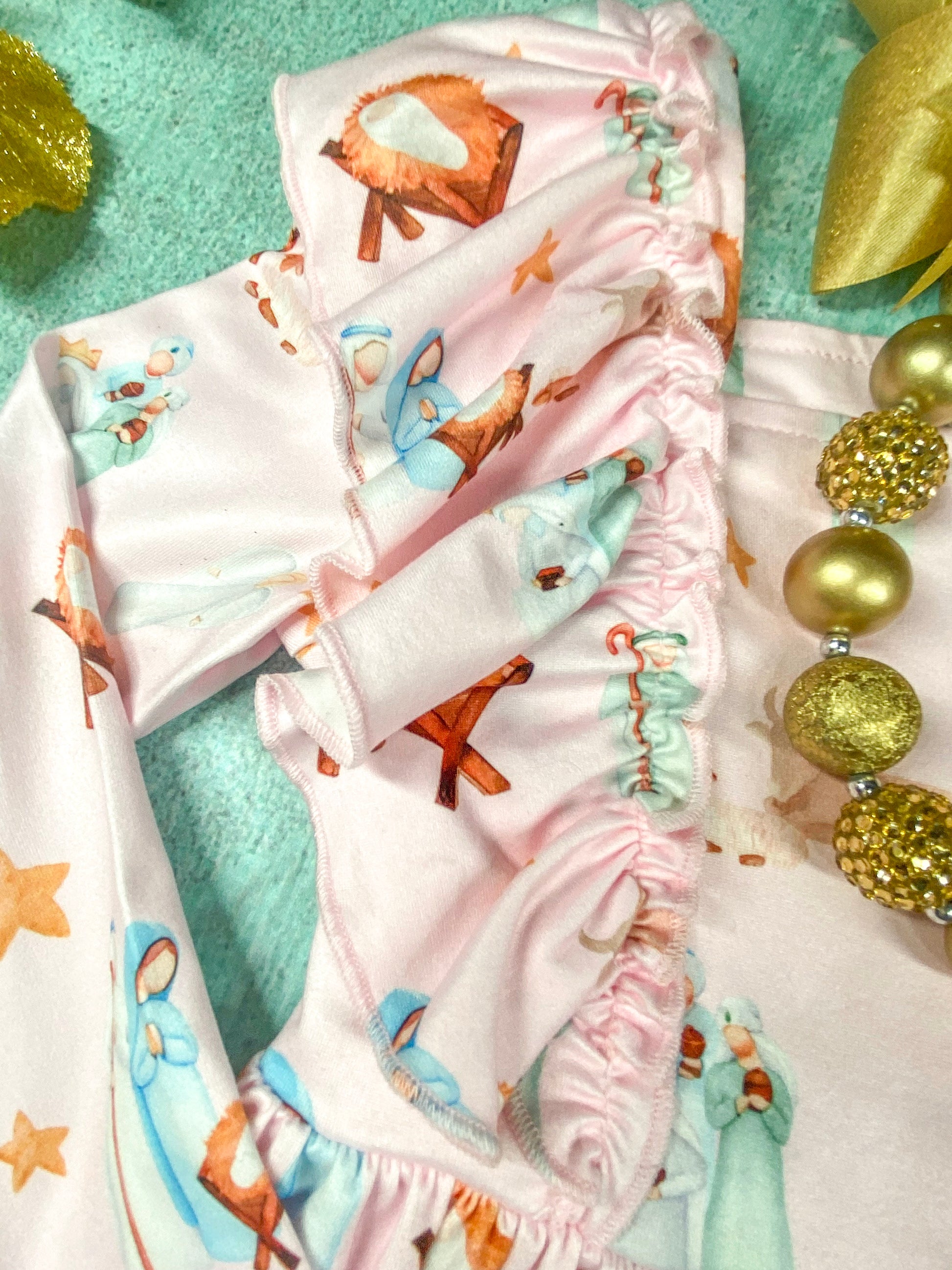 Close-up of the ruffled shoulder detail on a soft pink long sleeve dress with a nativity scene print, showing Mary, Joseph, and baby Jesus in a manger.