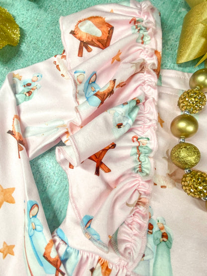 Close-up of the ruffled shoulder detail on a soft pink long sleeve dress with a nativity scene print, showing Mary, Joseph, and baby Jesus in a manger.