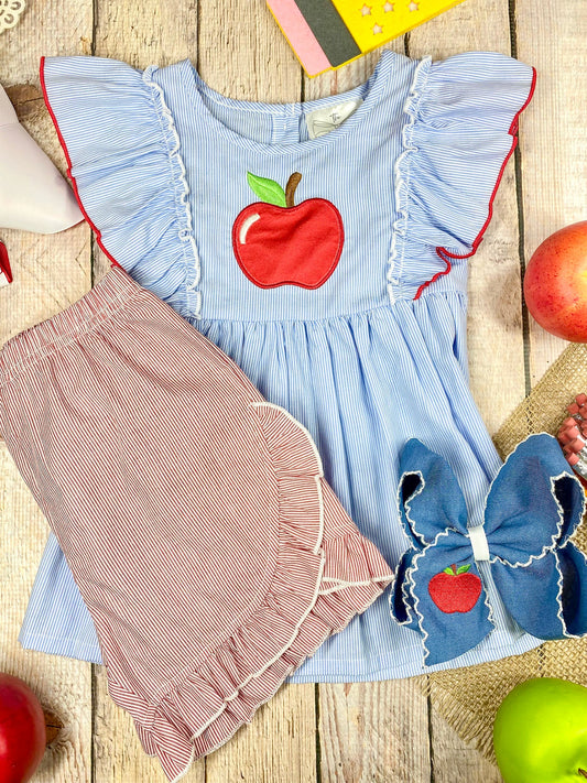 Children's outfit with blue top and pink shorts featuring an apple design on a wooden background