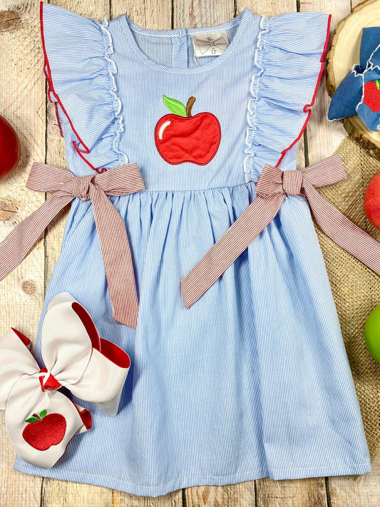 Blue dress with red apple design and pink accents on a wooden background