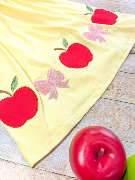 Yellow fabric with red apple and pink flower appliqués on a wooden surface. - Alternative view