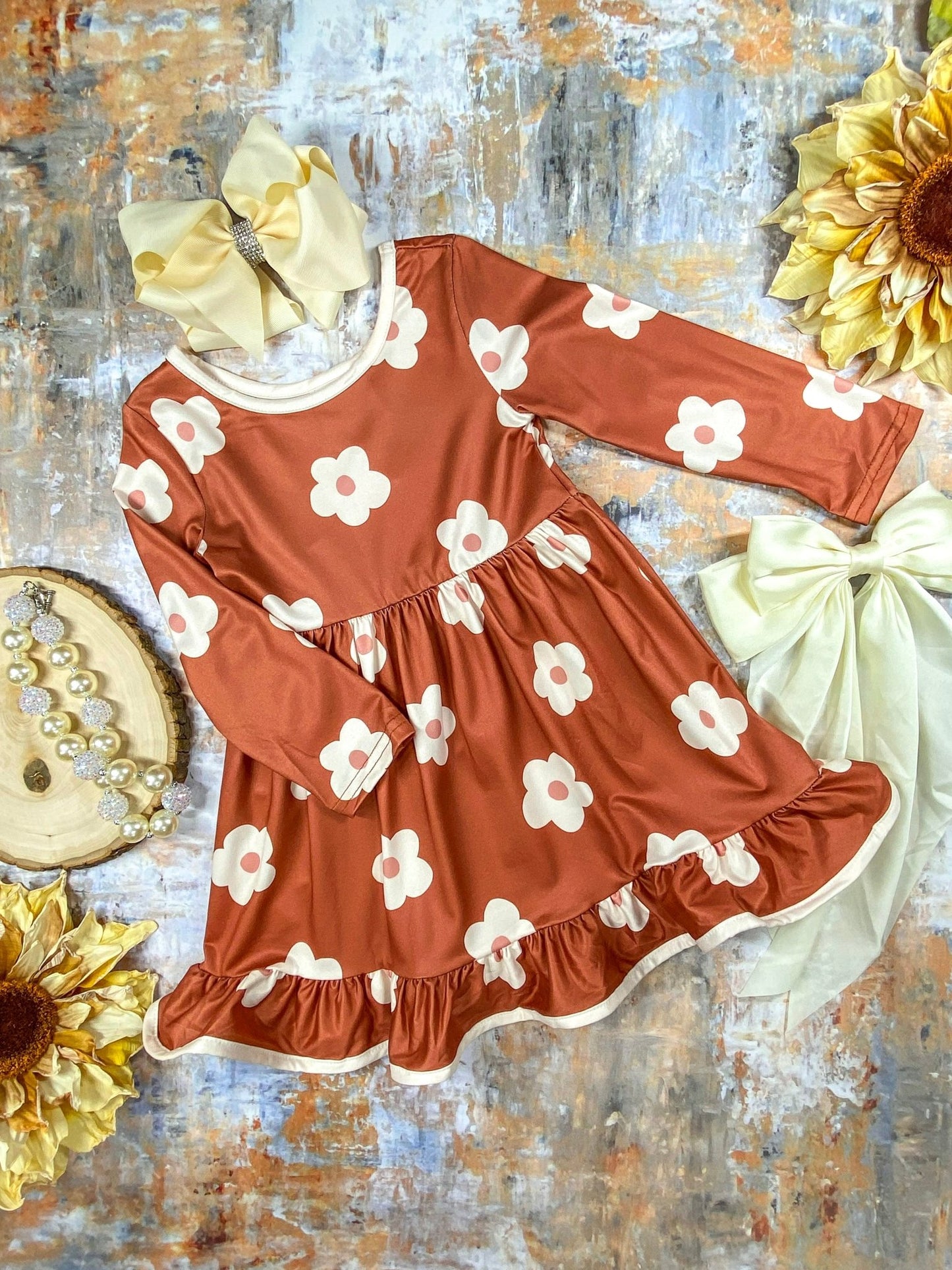 Brown dress with white floral pattern on a textured surface with dasies and ribbons.