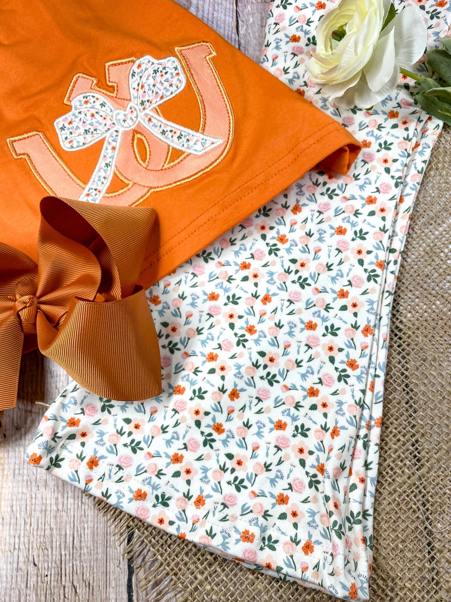 Girl wearing an orange horseshoe top with lace details and floral pants on a white background on a wooden background