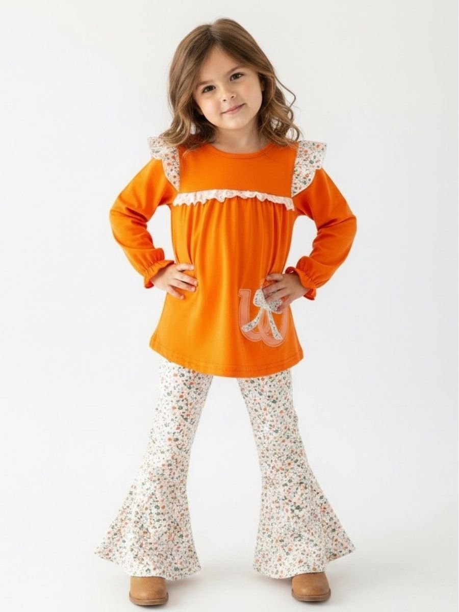 Girl wearing an orange horseshoe top with lace details and floral pants on a white background